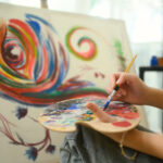 Close up of female artist mixing paint on a palette while working on her painting in studio